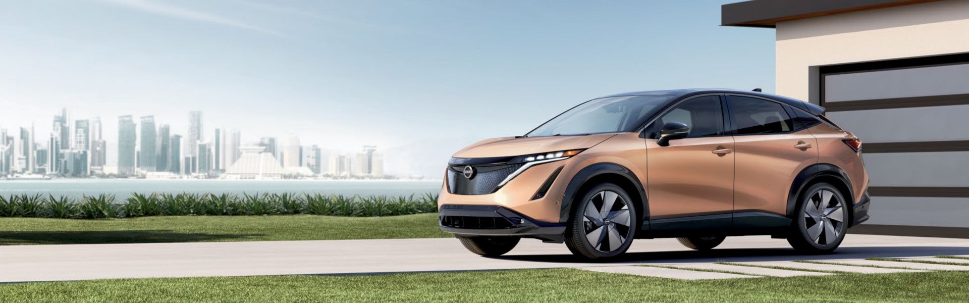 Nissan Ariya parked surrounded by grassy surface beside a river and buildings view
