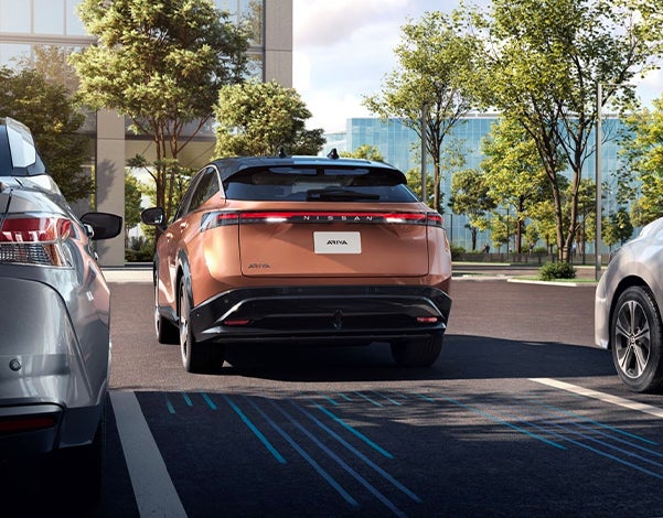 Nissan Ariya parked between two vehicles surrounded by trees beside a building